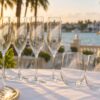 Laser-etched champagne flutes and stemless wine glasses with frosted palm frond designs on a waterfront wedding reception table