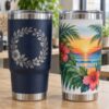 Navy tumbler with silver laser-engraved floral wreath beside a white tumbler with a full-color UV printed tropical sunset wrap