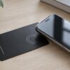 Black laser engraved metal NFC business card next to a smartphone on a wooden desk